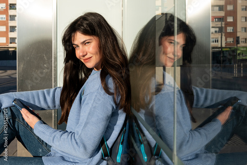 Confident woman sitting outdoors with smartphone and reflection photo