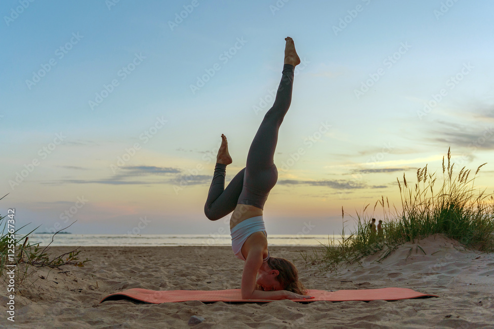 Fototapeta Practicing yoga in a headstand position on the beach during sunset with a tranquil atmosphere