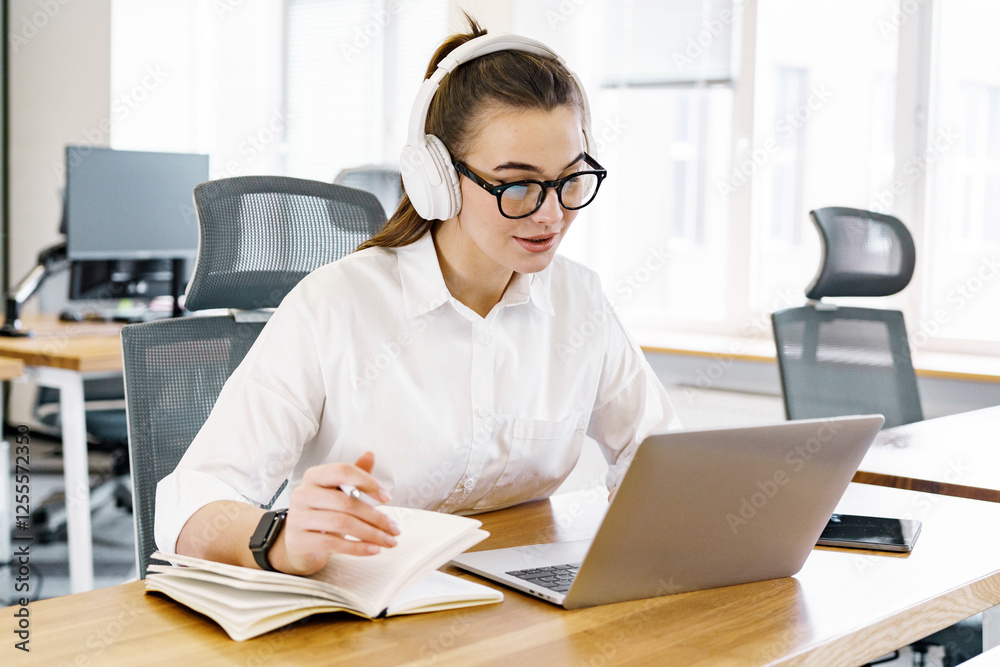 Young woman studying in a modern workspace, intensely focused on her laptop and notes Young woman studying in a modern workspace, intensely focused on her laptop and notes