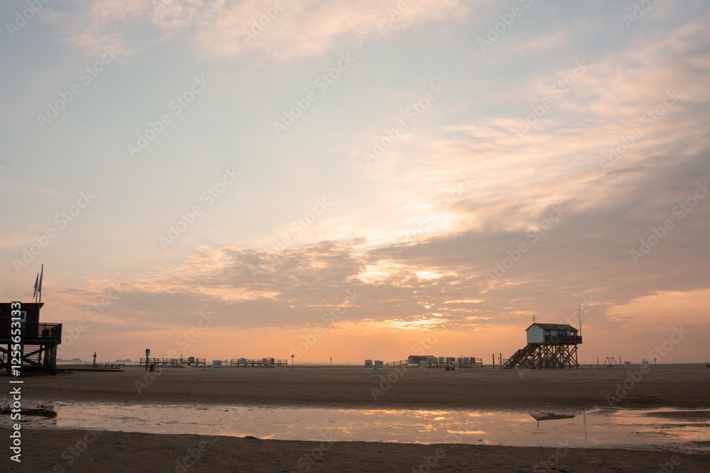 Breiter Sandstrand mit Pfahlbau in St. Peter-Ording an der Nordsee bei Sonnenaufgang.