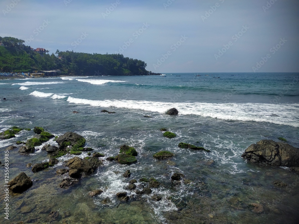 A beach with gentle waves, mossy rocks, and green hills in the distance. Fishing boats line the shore, creating a serene and natural coastal atmosphere. A beach with gentle waves, mossy rocks, and green hills in the distance. Fishing boats line the shore, creating a serene and natural coastal atmosphere.