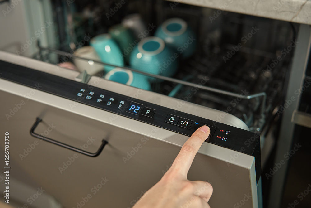 Close-up of female finger pressing button on dishwasher control panel. Woman using dishwasher in modern kitchen. Modern kitchen appliance with digital settings for efficient dishwashing