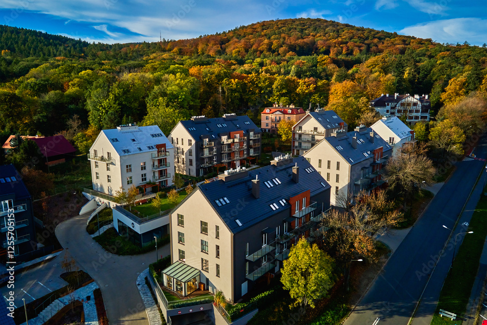 Residential building facade with balconies and windows near vibrant autumn forest, aerial view. Contemporary apartments in suburban eco friendly neighborhood with green spaces near mountains Residential building facade with balconies and windows near vibrant autumn forest, aerial view. Contemporary apartments in suburban eco friendly neighborhood with green spaces near mountains