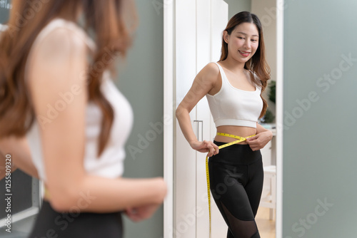 Happy Young women measure her body and look in the mirror and are proud of her loss weight program.