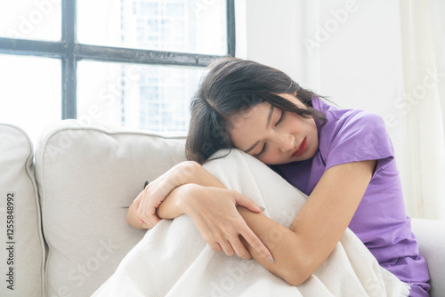 Free Download Sad and tired young Asian woman resting on a cozy sofa, emotional exhaustion, melancholic mood, wearing a purple shirt, feeling down, bored and stressed, peaceful but reflective moment - GFXLoad