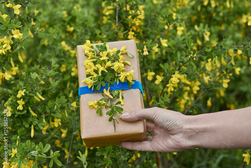 Gift wrapped with yellow flowers against a lush green background during a sunny day