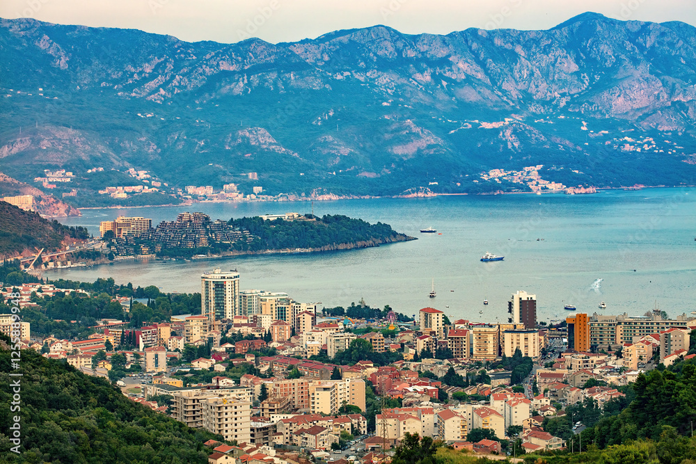 Breathtaking coastal view of a vibrant city Budva nestled by majestic mountains at sunset.