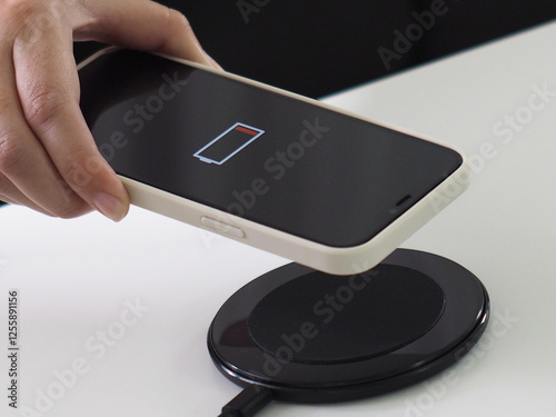 Charging mobile phone battery with wireless charging device in the table. Smartphone charging on a charging pad. Mobile phone near wireless charging