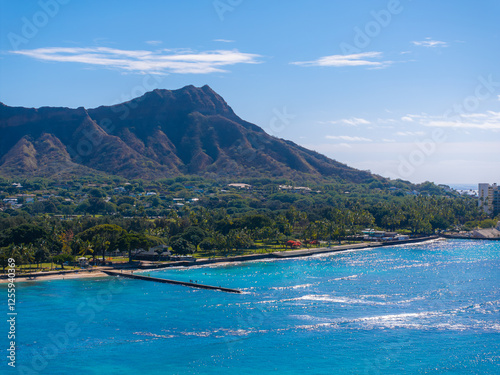 Aerial view of Diamond Head Crater on Oahu island, with turquoise waters, sandy beach, seawall, lush greenery, and scattered buildings in Honolulu.