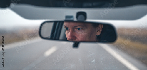 Female driver face at car rear view mirror on a rainy day