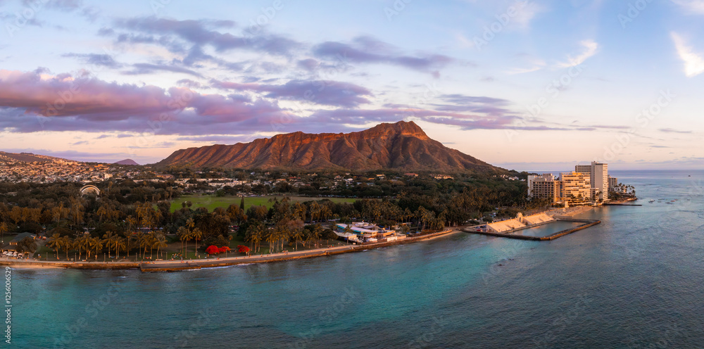 Fototapeta premium Aerial view of Diamond Head Crater on Oahu Island, Hawaii, at sunset. Turquoise waters, palm lined shore, and high rise buildings are visible.