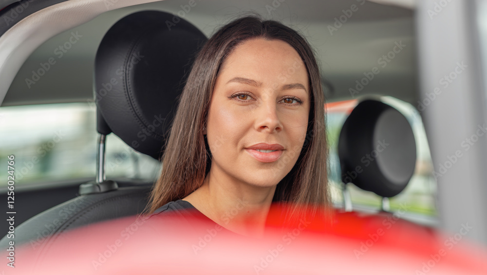 A young woman with long brown hair and a confident smile sits in the drivers seat of a modern car, looking forward with a relaxed expression.