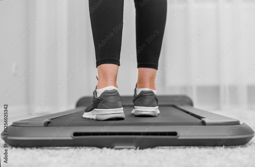 A person wearing black leggings and gray sneakers is walking on a compact treadmill in a modern, minimalistic home environment, focusing on fitness and an active lifestyle.