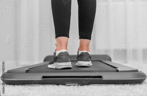 Obraz na płótnie A person wearing black leggings and gray sneakers is walking on a compact treadmill in a modern, minimalistic home environment, focusing on fitness and an active lifestyle. w salonie