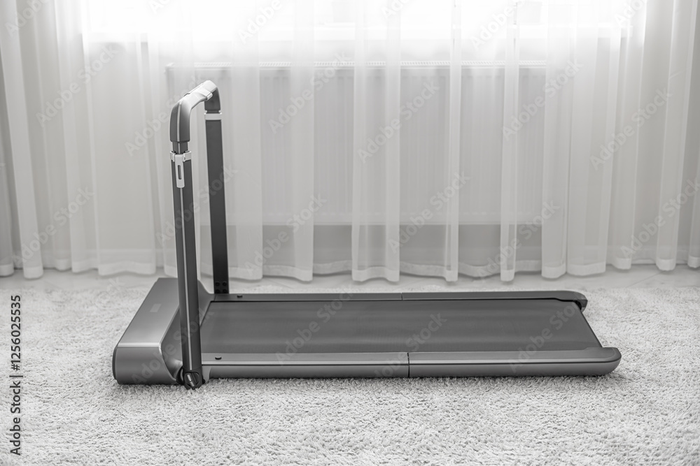 A modern, compact treadmill with a foldable handlebar is placed on a soft carpet in a bright, minimalistic home interior, designed for convenient indoor workouts.