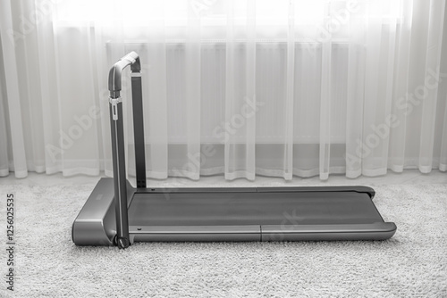 Obraz na płótnie A modern, compact treadmill with a foldable handlebar is placed on a soft carpet in a bright, minimalistic home interior, designed for convenient indoor workouts. w salonie