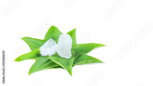 Pieces of alum stone on green leaf against white background. This image emphasizes the connection between natural minerals and plant based ingredients in traditional practices and holistic wellness.