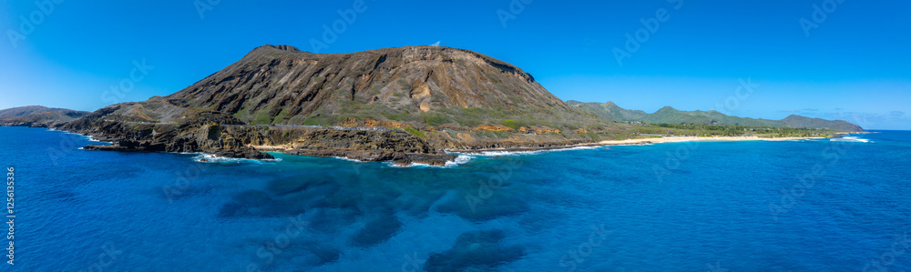 Aerial view of a volcanic mountain with rugged slopes near the shoreline on Oahu Island, Hawaii, featuring sandy beaches, a winding road, and clear skies. Aerial view of a volcanic mountain with rugged slopes near the shoreline on Oahu Island, Hawaii, featuring sandy beaches, a winding road, and clear skies.
