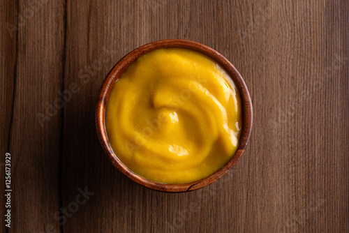 Mustard yellow sauce bowl on wooden background