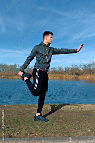 Man stretching outdoors beside lake on a sunny day