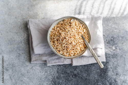 Top view of a bowl of chopped hazelnuts on a textured surface photo