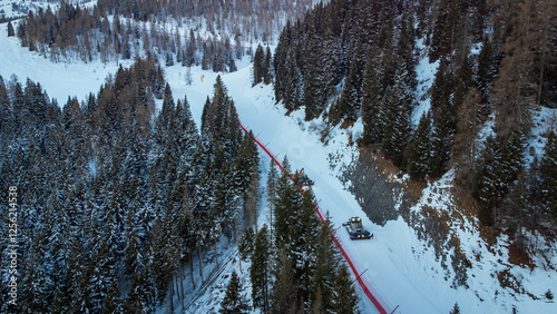 Two snowcats preparing ski slopes. Aerial view of the two vehicles between trees in the mountains in winter photo