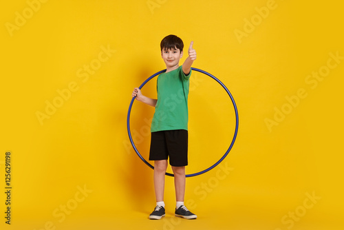 Boy with hula hoop showing thumbs up on yellow background photo