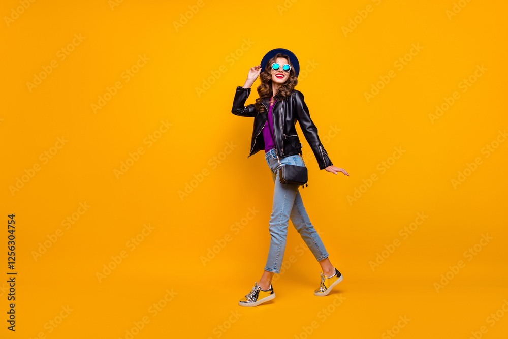 Full size photo of charming content girl enjoying promenade have fun wear black leather look outfit denim jeans isolated over yellow color background Full size photo of charming content girl enjoying promenade have fun wear black leather look outfit denim jeans isolated over yellow color background