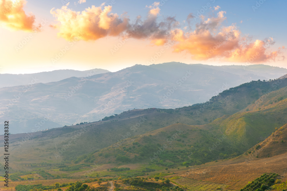 Naklejka premium scenic rustic landscape with green hills and farms in a mountain valley during colorful cloudy sunset