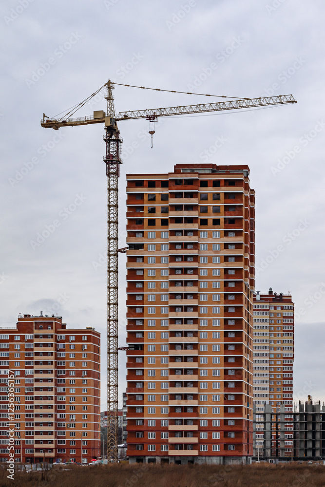 Construction crane working on high-rise residential building under cloudy sky at urban development site Construction crane working on high-rise residential building under cloudy sky at urban development site