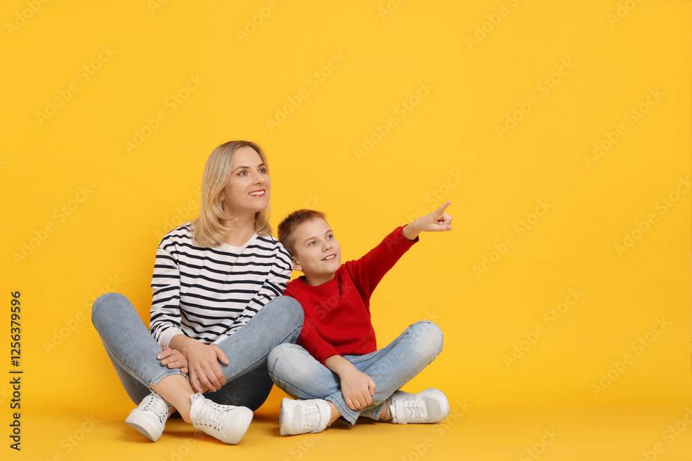 Son showing his mother something on orange background. Space for text Son showing his mother something on orange background. Space for text