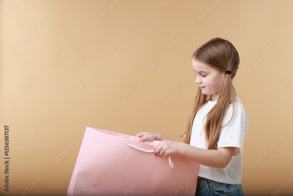 Cute little girl with shopping bag on beige background. Space for text Cute little girl with shopping bag on beige background. Space for text