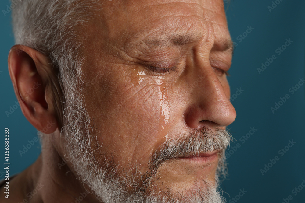 Fototapeta premium Sad senior man crying on blue background, closeup
