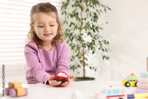 Little girl playing with toy cars at white table indoors, space for text
