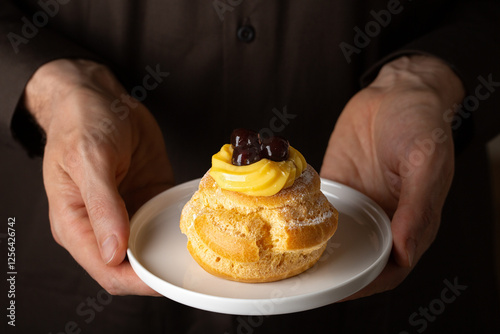 Close up of Man hands holding Italian dessert Zeppole di San Giuseppe or  zeppola, fathers day pastry symbol.  Baked puffs made from choux pastry, filled and decorated with custard cream and cherry. photo