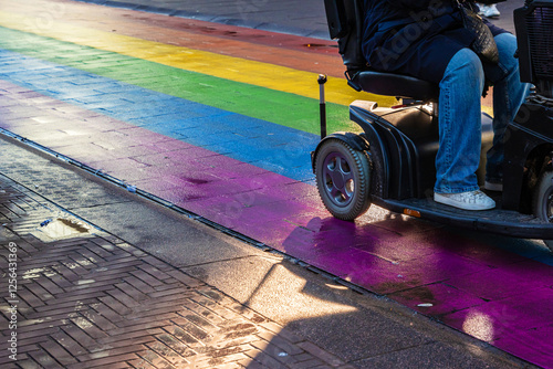 Person using a mobility scooter on a rainbow crosswalk on Regenboogvlag in the Grote Marktstraat. Rainbow street in the center of the Hague, Netherlands. Selective focus.

