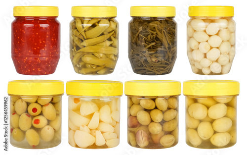 Different canned pickles in transparent jars with yellow lids: olives, chili sauce, okra, onions, sea fennel, green olives, garlic. photo