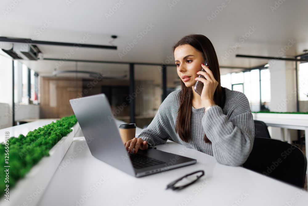 Portrait of executive woman sitting at desk and working on laptop while making call. Portrait of executive woman sitting at desk and working on laptop while making call.