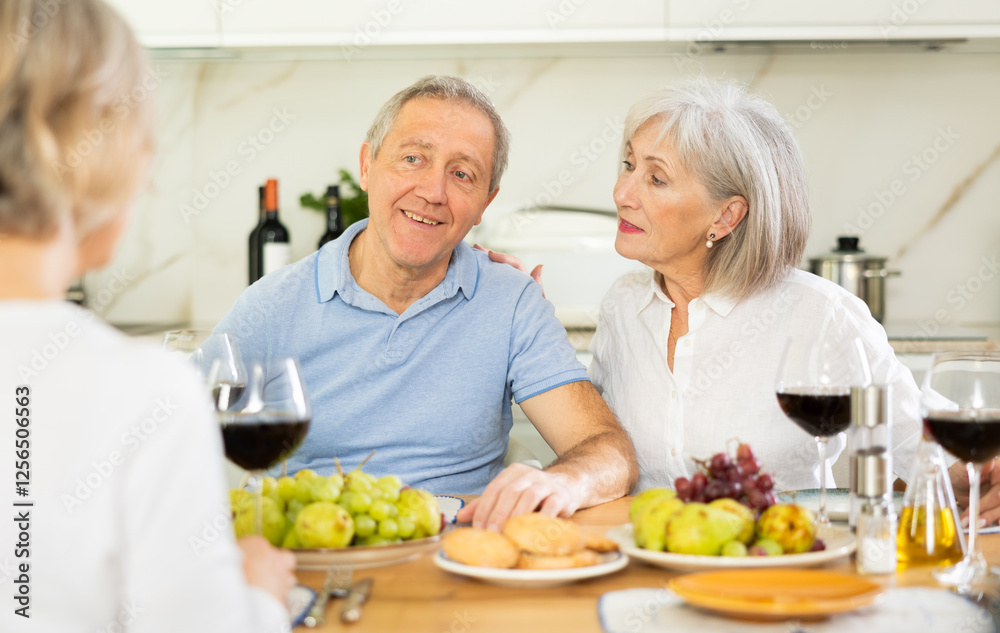 Two elderly women and elderly man chatting and drinking wine at table.. Two elderly women and elderly man chatting and drinking wine at table..