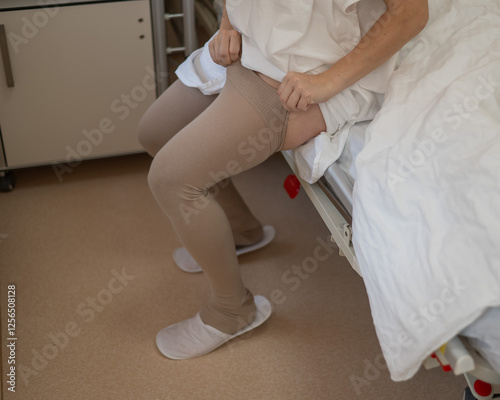 A woman puts on post-operative compression stockings in a hospital room. 