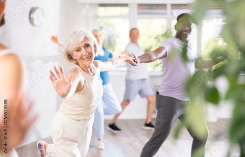 Cheerful elderly woman practicing vigorous lindy hop moves paired with african american male partner in dance class. Social dancing concept photo