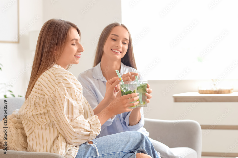 Beautiful young happy women with glasses of mojito sitting on sofa at home