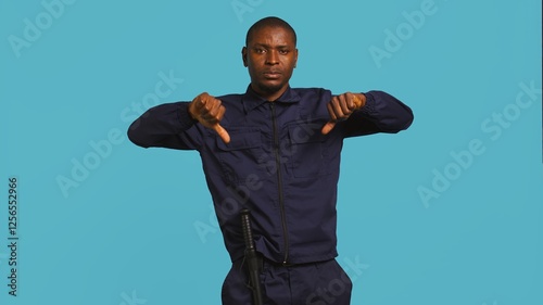 Portrait of security guard doing thumbs down sign gesturing, denying access while overseeing premises. Private law enforcement worker doing negative hand gesture, studio backdrop, camera B photo