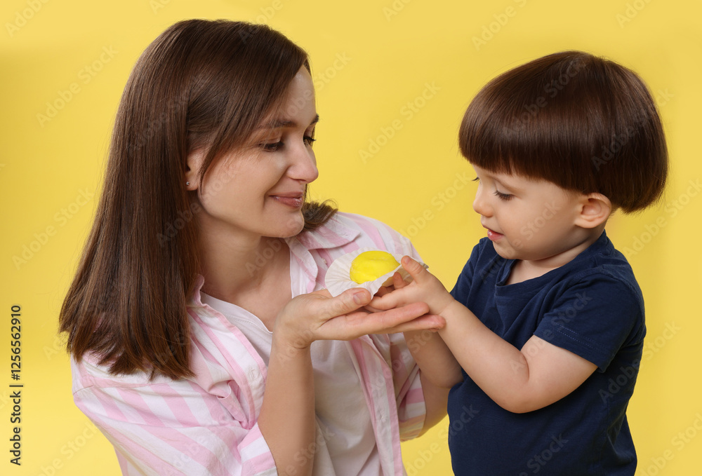 Mother and baby eating tasty mochi on yellow background Mother and baby eating tasty mochi on yellow background