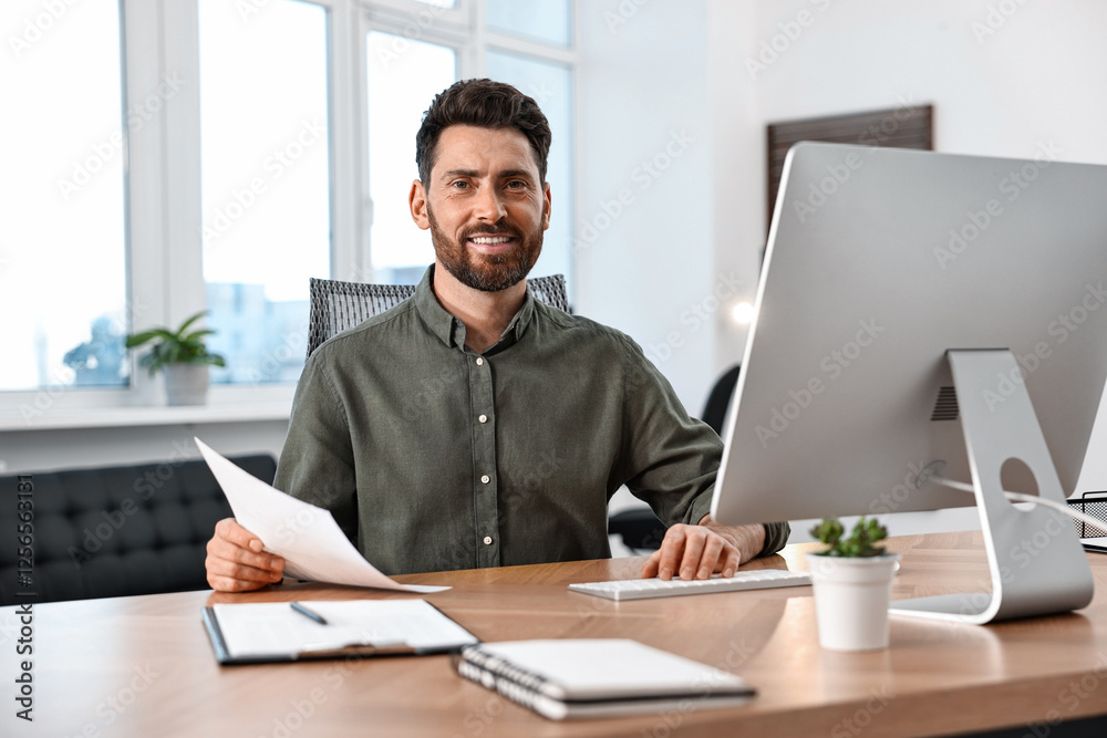 Man with document working on computer at table in office Man with document working on computer at table in office