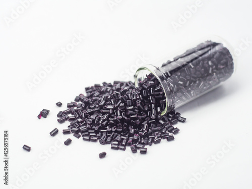 Transparent black masterbatch granules spilling from glass tube on white background, polymer carrier of color pigment in plastic industry. Perfect for plastic company catalog design