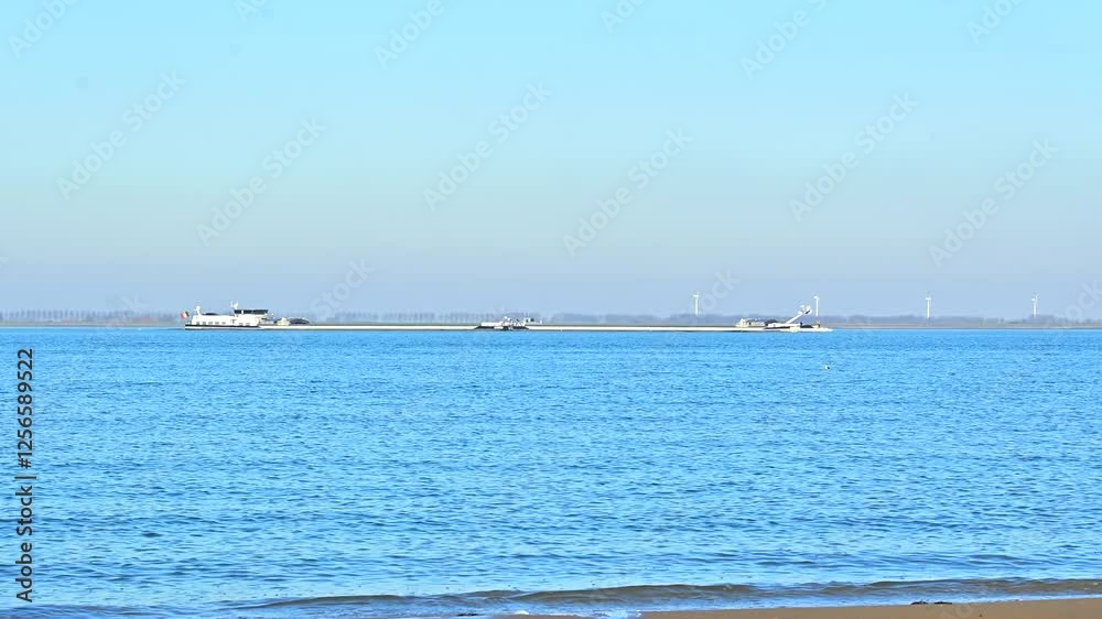 seascape view with long inland cargo vessel sailing in the North Sea and wind mills on horizon
seascape view with long inland cargo vessel sailing in the North Sea and wind mills on horizon