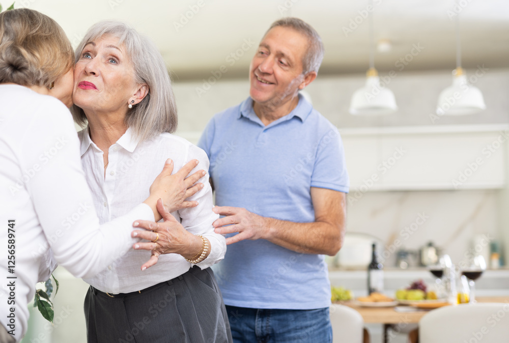 Fototapeta premium Two elderly women friends hugging when meeting in kitchen