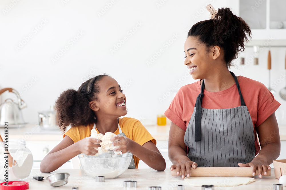 Joyful african american mother and daughter baking together at home, making dough for cookies and having pleasant conversation, blending and rolling dough, enjoying weekend together, copy space Joyful african american mother and daughter baking together at home, making dough for cookies and having pleasant conversation, blending and rolling dough, enjoying weekend together, copy space