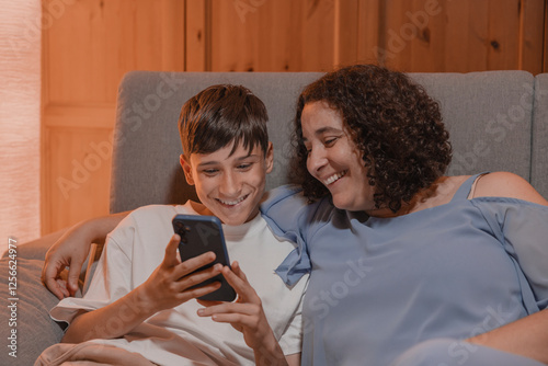 A young boy and girl are sitting on a couch, both looking at a cell phone